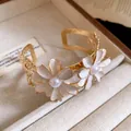 Detailed view of an elegant gold cuff bracelet with white enamel daisy flowers and pearls. - Beige