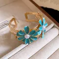 Detail view of a luxury gold cuff bracelet featuring blue enamel flowers and pearls. - Blue