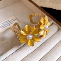Detailed view of the yellow enamel flowers and pearl centers on gold-tone cuff bracelet. - Yellow
