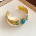 Close-up view of a vintage gold-tone cuff bracelet featuring oval turquoise stones - Cuff Bracelet / Gold