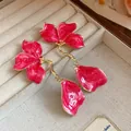 Close-up view of elegant pink enamel flower drop earrings in a velvet jewelry box. - Rose Red