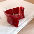 Detailed close-up of a red marbled resin bracelet with an irregular geometric twisted design. - Bangle / Burgundy