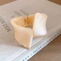 Close-up of cream resin bangle with marbled texture and gold hinged clasp on a book - Bangle / Khaki