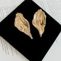 Close-up of textured gold leaf earrings with an irregular wrinkled metal design. - Gold