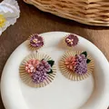 Detailed macro view of elegant fabric flower earrings with golden sunburst frame - Purple