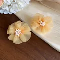 Dettaglio di orecchini a fiore in chiffon color albicocca con piccoli pistilli di perle - Giallo