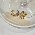 Primer plano de ear cuffs dorados con circonitas y diseño cruzado sobre fondo blanco. - Ear Cuffs Cruzados de Tres Capas (Juego de Dos Piezas) / Dorado