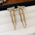 Close-up of gold-plated bow earrings with sparkling zircon tassels in jewelry box. - Bow Tassel / Gold