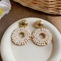 Elegant golden textured stud earrings featuring a circular white pearl drop design - Pink