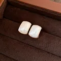 Détail rapproché d'élégantes boucles d'oreilles en résine crème avec cadre doré en boîte. - Carré / Or