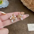 Detailed view of elegant gold-tone camellia earrings with zircons and white petals - Ear Buckle / Gold and White