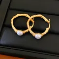Macro close-up detail of textured golden hoop earrings featuring elegant white pearls - Round Wrinkle Style / Gold