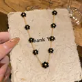 Detailed view of a gold-tone necklace with delicate black beaded flowers on textured paper. - Choker Necklace / Gold-Black