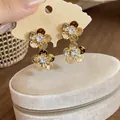 Close-up detail of elegant gold flower drop earrings with sparkling zircon center stones - Gold