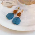 Primer plano de pendientes geométricos de resina veteada azul sobre fondo de concha blanca - Azul