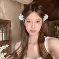 Barrettes à fleurs en tissu bleu et blanc portées par un mannequin pour un look de vacances - Bleu