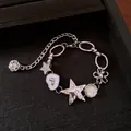 Détail d'un bracelet punk argenté avec des breloques étoile et cœur en strass sur noir. - Style Multi-Breloques Punk / Argent