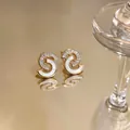 Primer plano detallado de pendientes de oro con nácar y circonitas baguette muy elegantes. - Estilo Remolino en S / Dorado