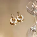 Primer plano de elegantes pendientes de aro dorados con nácar blanco y circonitas - Estilo de Anillo Circular / Dorado