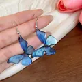 Close-up detail of translucent blue resin butterfly earrings with fine glitter and silver hooks - Hook Style / Blue