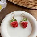 Detailed macro view of handmade red beaded strawberry hook earrings on a white plate. - Hook-Red (HE32481)