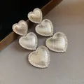 Macro view of textured silver-tone triple heart drop earrings on a neutral background - Silver