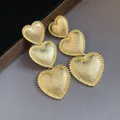 Detailed macro shot of elegant golden tiered heart drop earrings with textured finish - Gold
