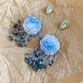 Nahaufnahme eleganter blauer Harz-Rosenohrringe mit Perlenquasten auf Vintage-Papiergrund. - Quasten-Stil / Blau