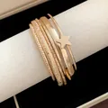Primo piano di un bracciale rigido dorato a più strati con stella su supporto bianco. - Set di Bracciali / Oro