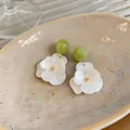 Close-up of elegant resin flower earrings with green beads on a textured ceramic plate. - Flower Shape / White & Green