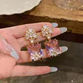 Eleganti orecchini pendenti con gemma rosa quadrata e grappoli di zirconi scintillanti. - Oro