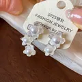 Dettaglio di orecchini a fiore asimmetrici con perle lucide su aghi in argento S925 - Fiore Asimmetrico (HE31773) / Bianco