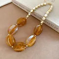 Detailed macro view of amber marbled acrylic beads and shiny gold-toned metal necklace - Necklace / Brown
