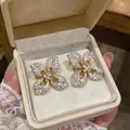 Detailed view of gold-tone silver needle flower stud earrings with crystals in a box - Gold