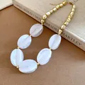 Macro view of white marbled acrylic beads and gold metallic spheres on a chunky necklace. - Necklace / White