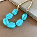 Detail view of chunky turquoise marbled acrylic beads on a gold-toned necklace. - Necklace / Cyan