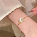 Detailed view of an elegant floral charm bracelet with shell inlay on a wrist. - Bracelet / Gold