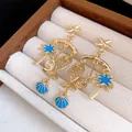 Close-up of ocean-themed drop earrings with gold starfish and blue enamel charms - Blue