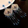 Close-up detail of intricate silver filigree earrings with blue glass waterdrop tassels. - Blue