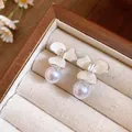 Close-up of elegant flower stud earrings with white pearls in a wooden jewelry box display - White