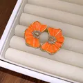 Primer plano de pendientes de flores de esmalte naranja con detalles de cristales. - Naranja