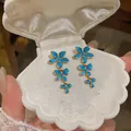 Detailed view of blue enamel flower tassel earrings in a white shell jewelry box - Blue