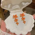 Macro detail of orange flower tassel earrings presented inside a white shell jewelry box. - Orange
