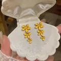 Detail of yellow enamel flower tassel earrings inside a white shell jewelry box. - Yellow