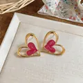 Detalle de pendientes de corazón dorados con esmalte rosa sobre soporte blanco. - Rosa
