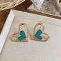 Primer plano de pendientes de corazón con esmalte azul turquesa y acabado dorado. - Azul
