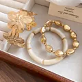 Detail of golden metal flower bangle and cream beaded bracelet set on velvet tray - Bangle and Bracelet Set / Gold-Beige