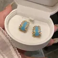 Close-up of vintage geometric gold earrings with turquoise stones in a white jewelry box. - Geometric Arch Micropave Style (HE32849)