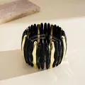 Macro view of black marbled acrylic and gold wavy segments on an elastic bracelet - Black