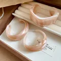 Dettaglio di tre bracciali geometrici in acrilico marmorizzato in un portagioie elegante - Rosa